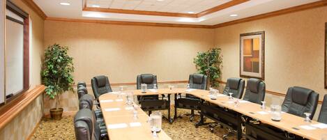 A conference room with a long table, multiple chairs, and potted plants.