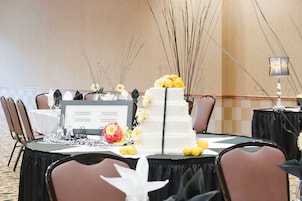 Una mesa para recepción de boda con un pastel blanco de varios pisos, decoraciones florales y un atril para el menú.