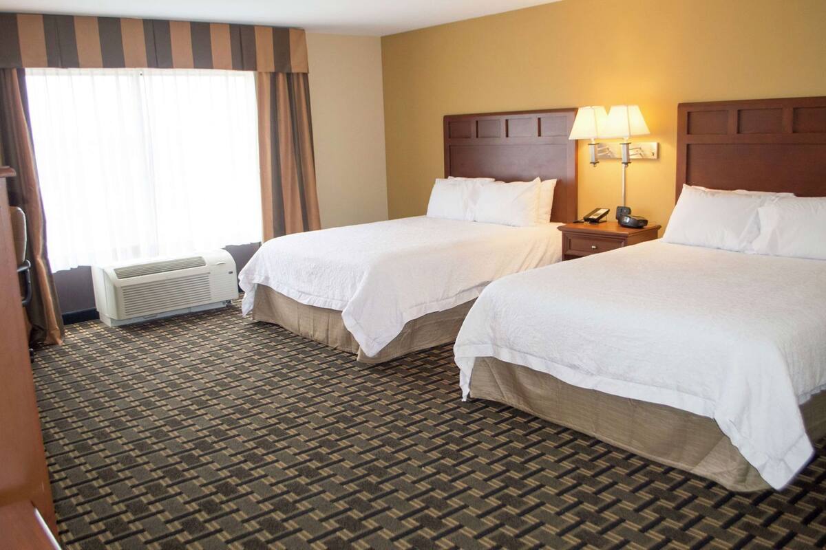 A hotel room with two beds, a bedside lamp, a phone, and a window with curtains.