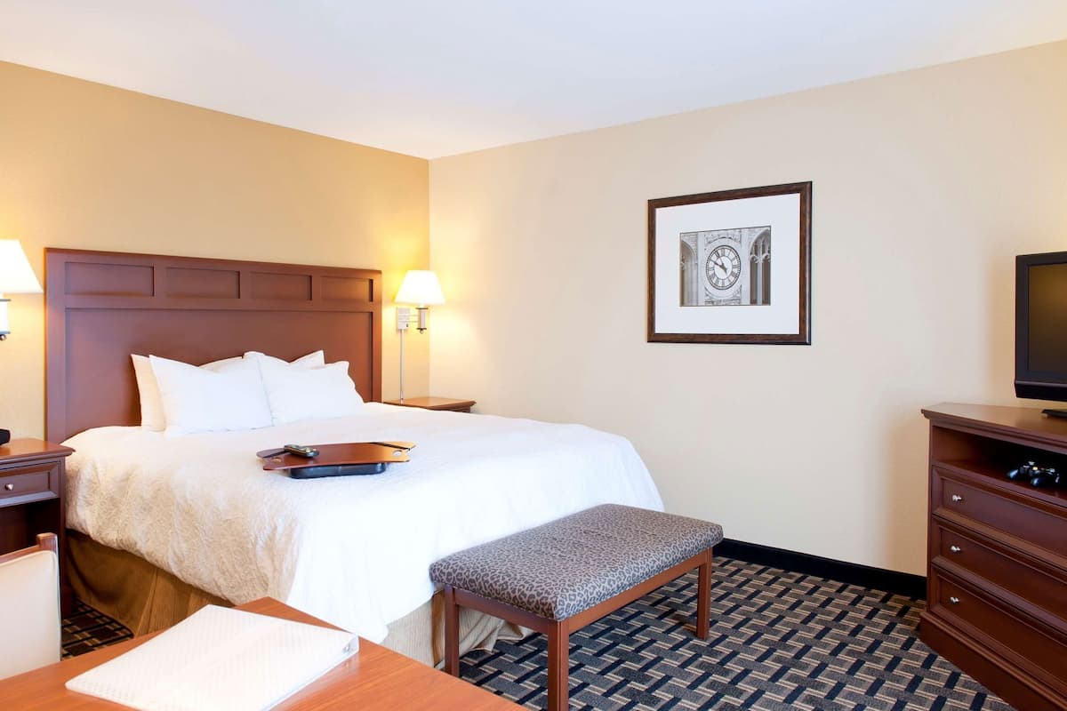 A hotel room with a bed, bedside tables, a desk, a chair, a television, and a framed picture on the wall.
