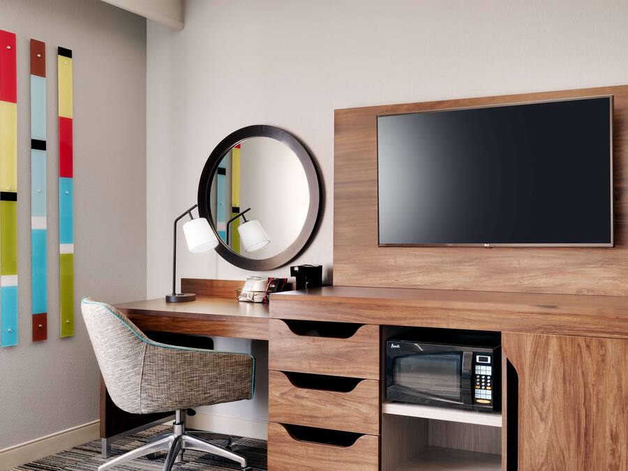 Un espacio de oficina moderno con un escritorio de madera, una silla, un espejo redondo, un televisor de pantalla plana y un microondas.