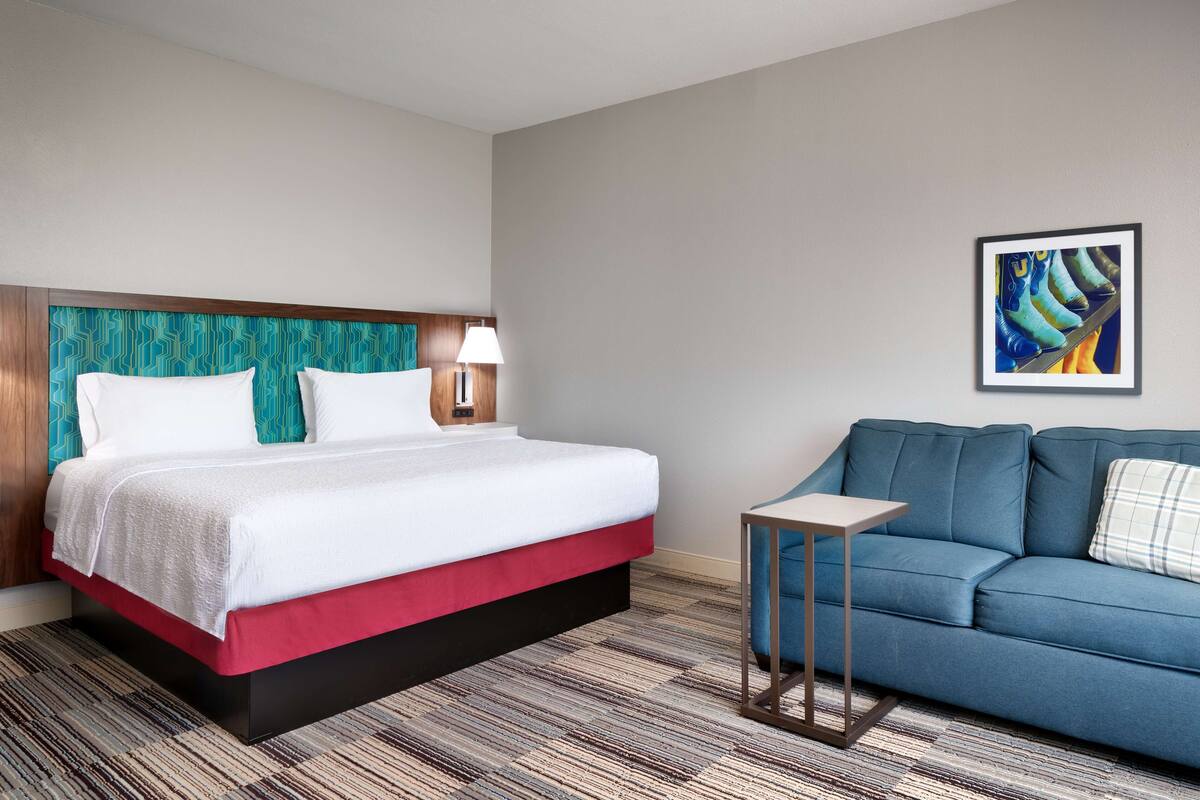 A hotel room with a bed, a blue sofa, a small table, and a painting on the wall.