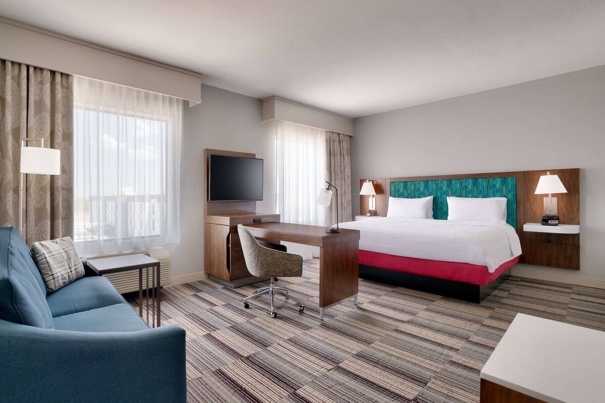 A hotel room with a bed, a desk, a chair, a TV, and a sofa.