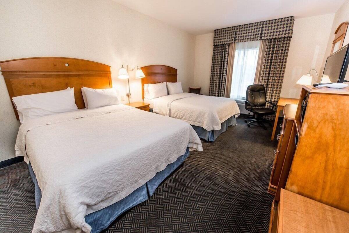 A hotel room with two beds, a desk, a chair, and a television.