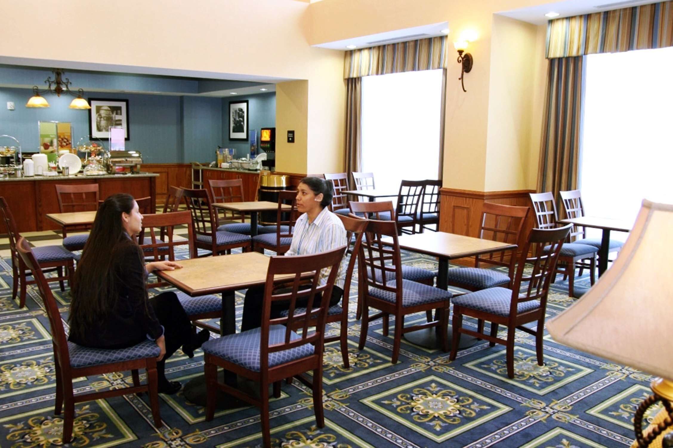 Un comedor de hotel con varias mesas y sillas, una barra de buffet y una alfombra estampada.