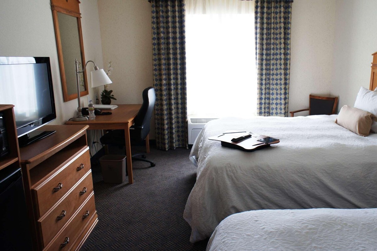 Une chambre d’hôtel avec un lit, un bureau avec un ordinateur, une télévision et une commode.