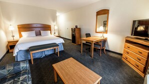 Een hotelkamer met een bed, nachtkastje, bankje, bureau, stoel, kast, televisie en een spiegel.