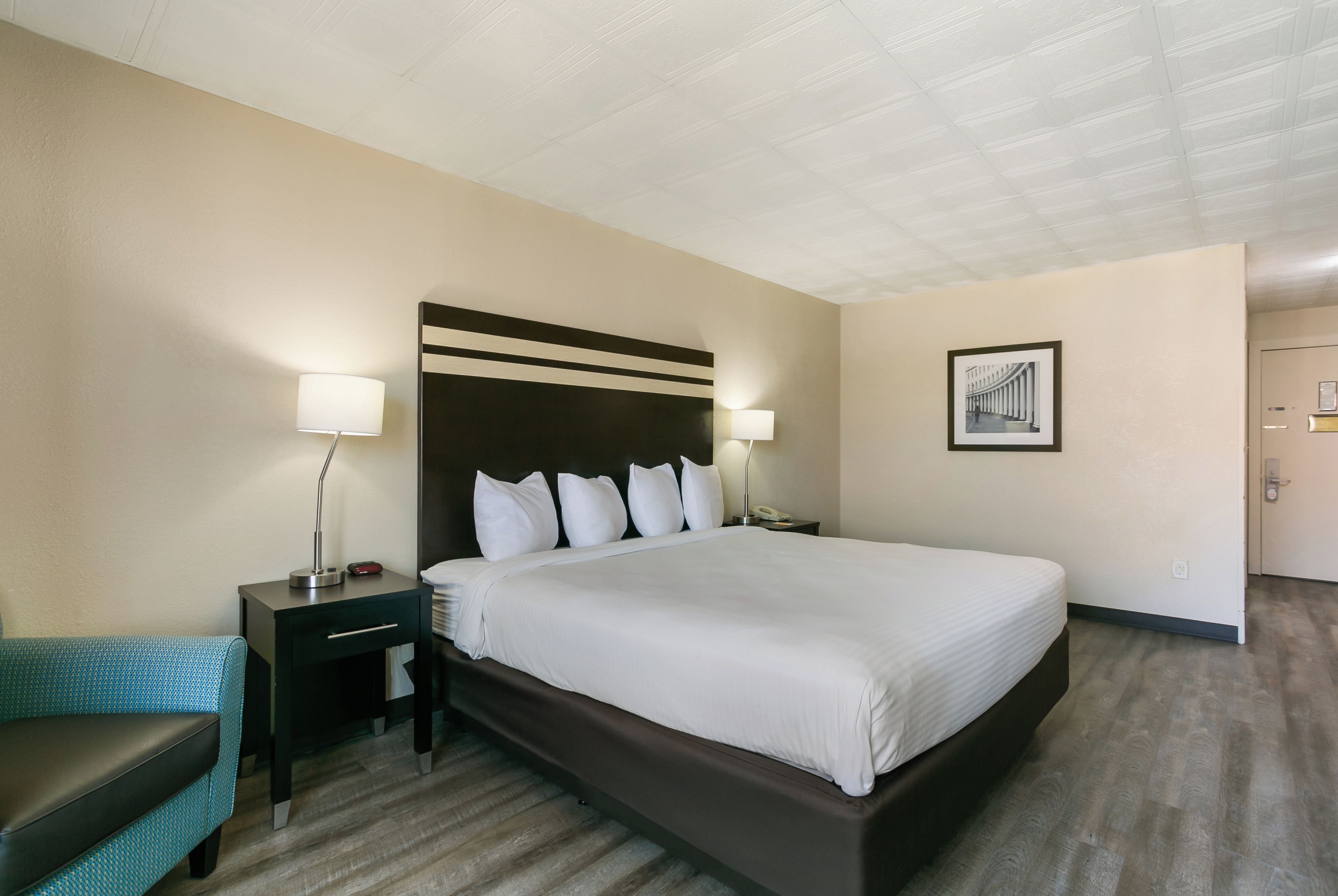 A hotel room with a large bed, two bedside tables with lamps, a chair, and a framed picture on the wall.