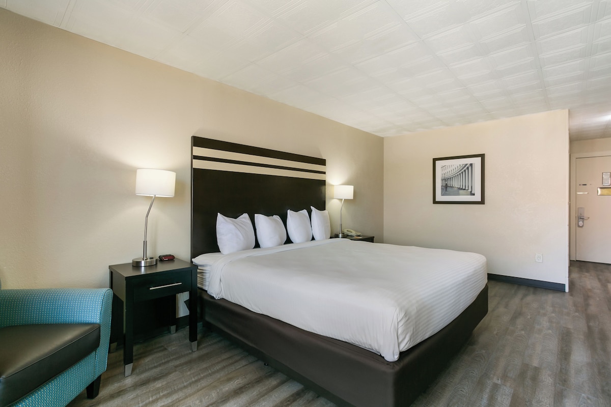 A hotel room with a large bed, two bedside tables with lamps, a chair, and a framed picture on the wall.