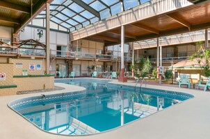 Piscina interior com vários níveis, rodeada por áreas de descanso e mobiliário de exterior.