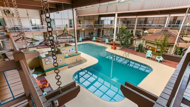 An indoor swimming pool with a glass bottom, surrounded by lounge chairs and tables, and multiple balconies with outdoor seating. - Eisenhower Hotel & Conference Center (Gettysburg)