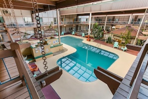 An indoor swimming pool with a glass bottom, surrounded by lounge chairs and tables, and multiple balconies with outdoor seating. - Eisenhower Hotel & Conference Center (Gettysburg)