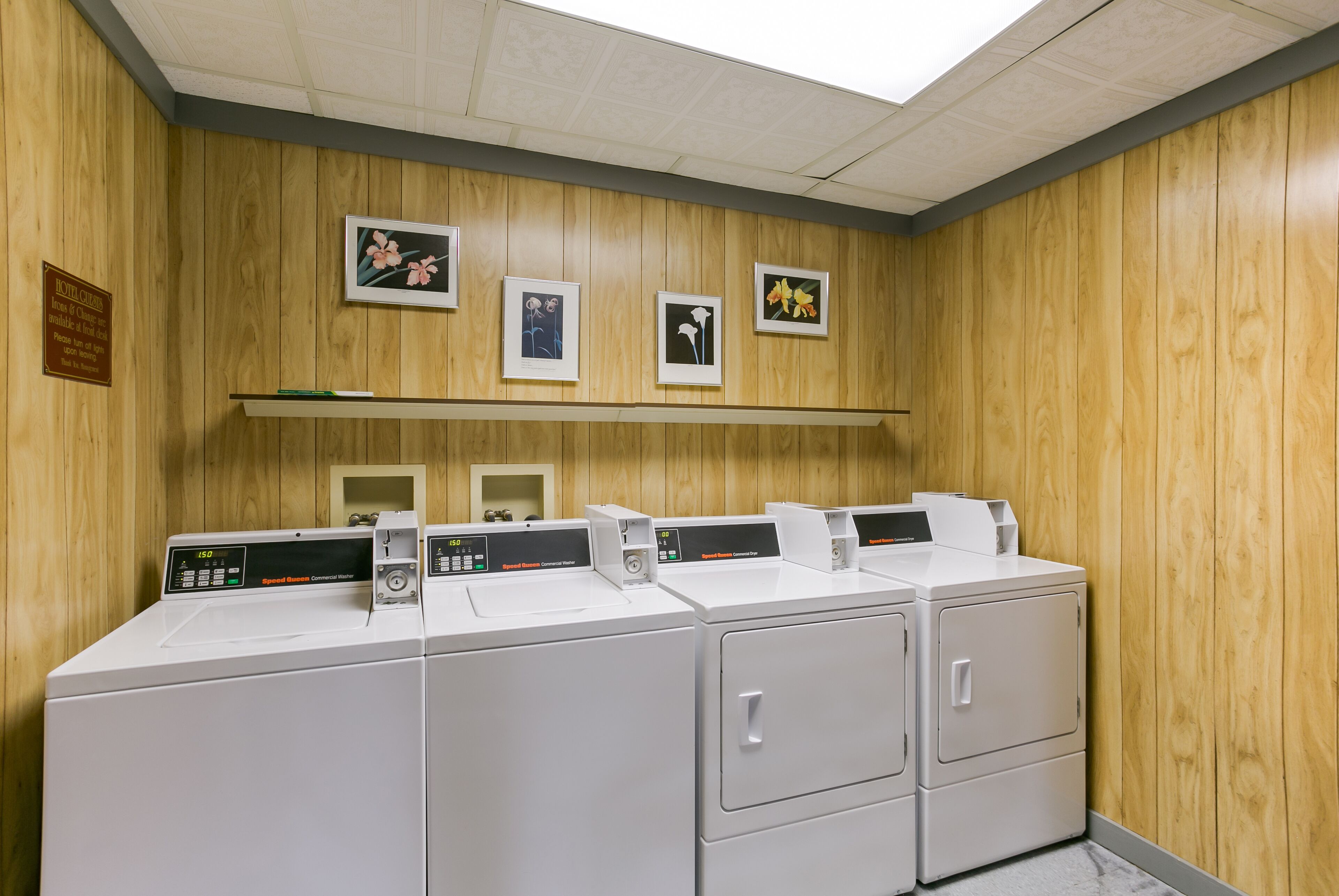 A laundry facility with four washers and dryers, wooden panel walls, and framed pictures on the wall.