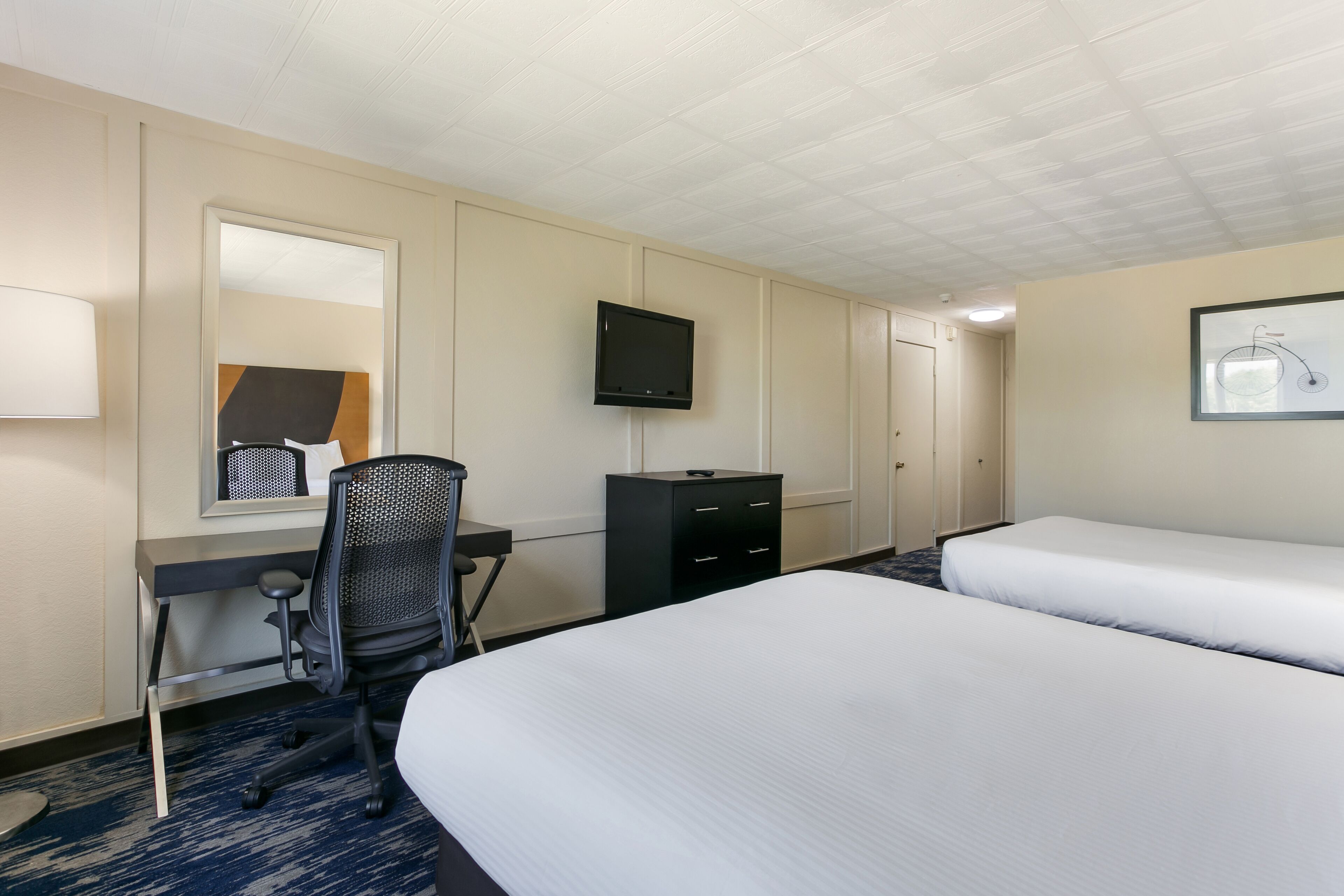 Une chambre d’hôtel comprenant un lit, un bureau avec une chaise, une télévision et une commode.