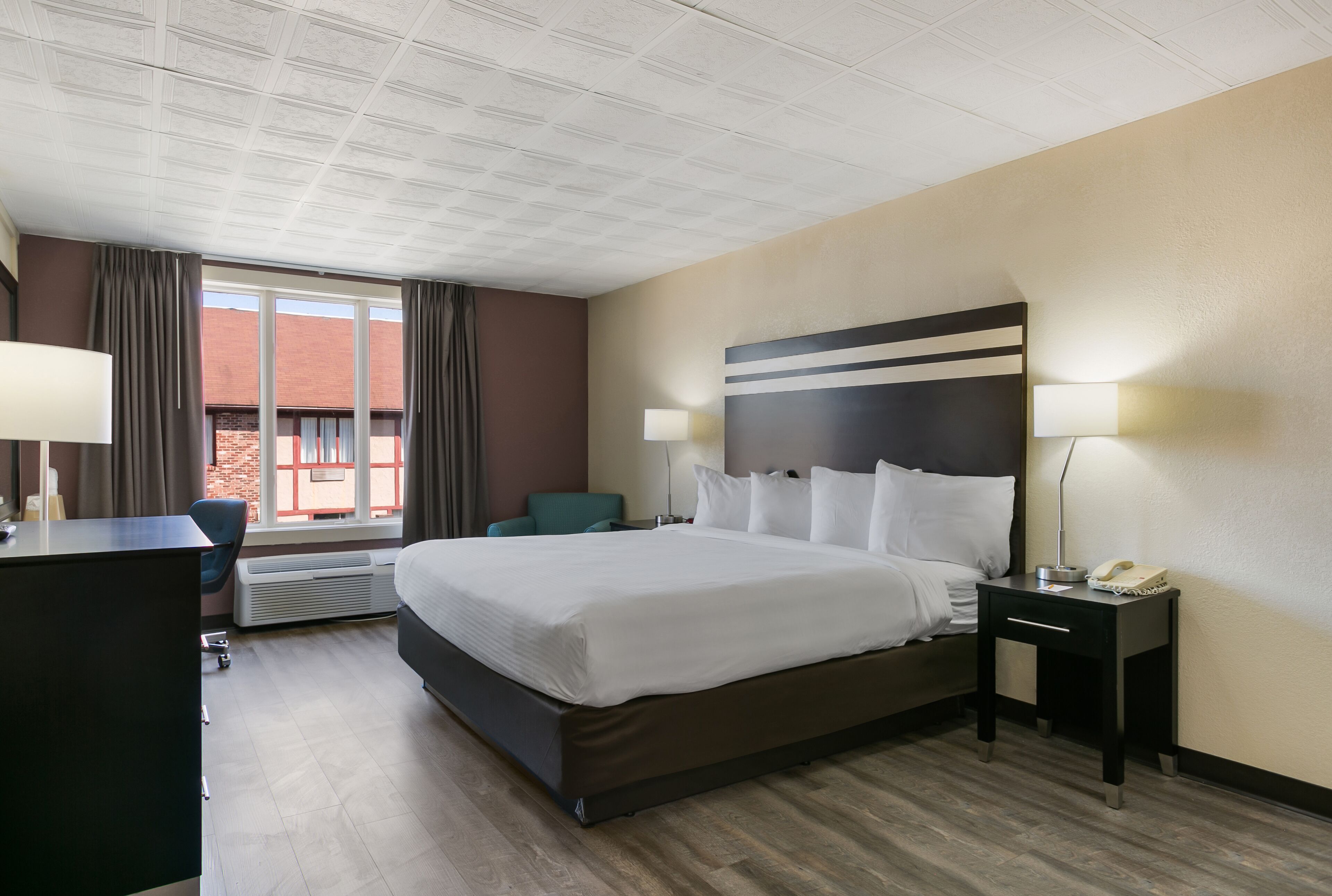 Quarto de hotel com uma cama grande, uma mesa, uma cadeira e vista para um edifício pela janela.