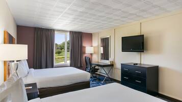Habitación de hotel con dos camas, un escritorio, una silla, un televisor y una ventana con cortinas.