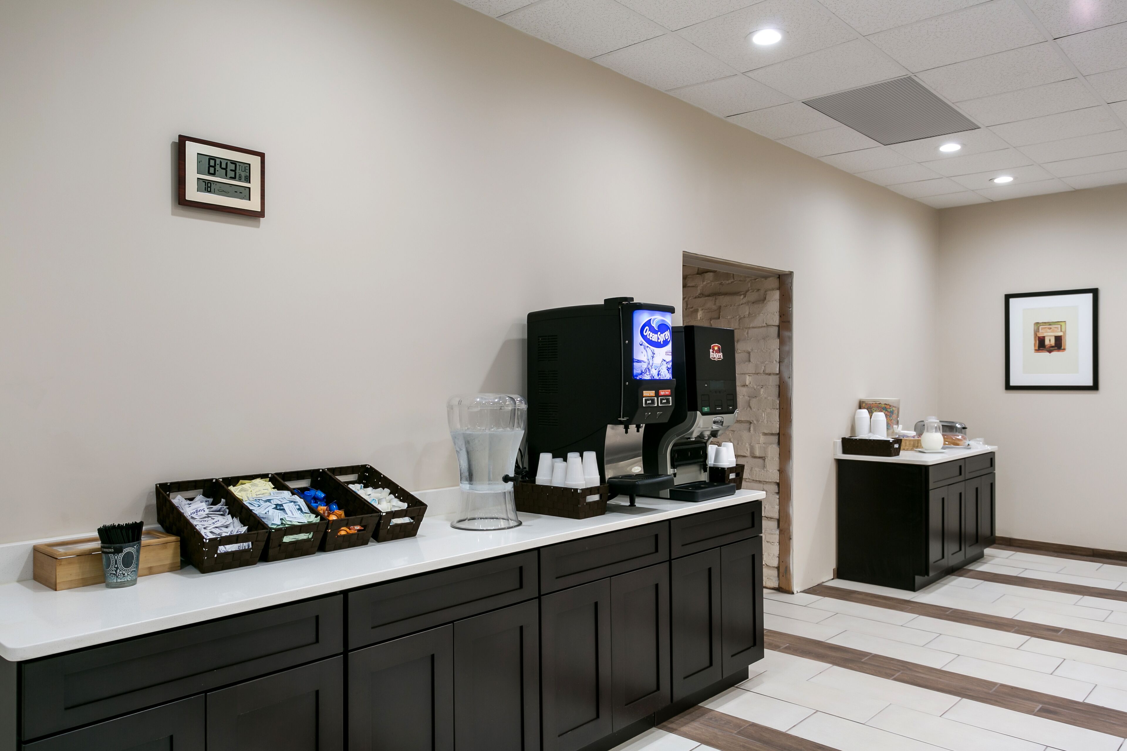 A reception area with a digital clock, coffee machine, and various amenities on a counter.