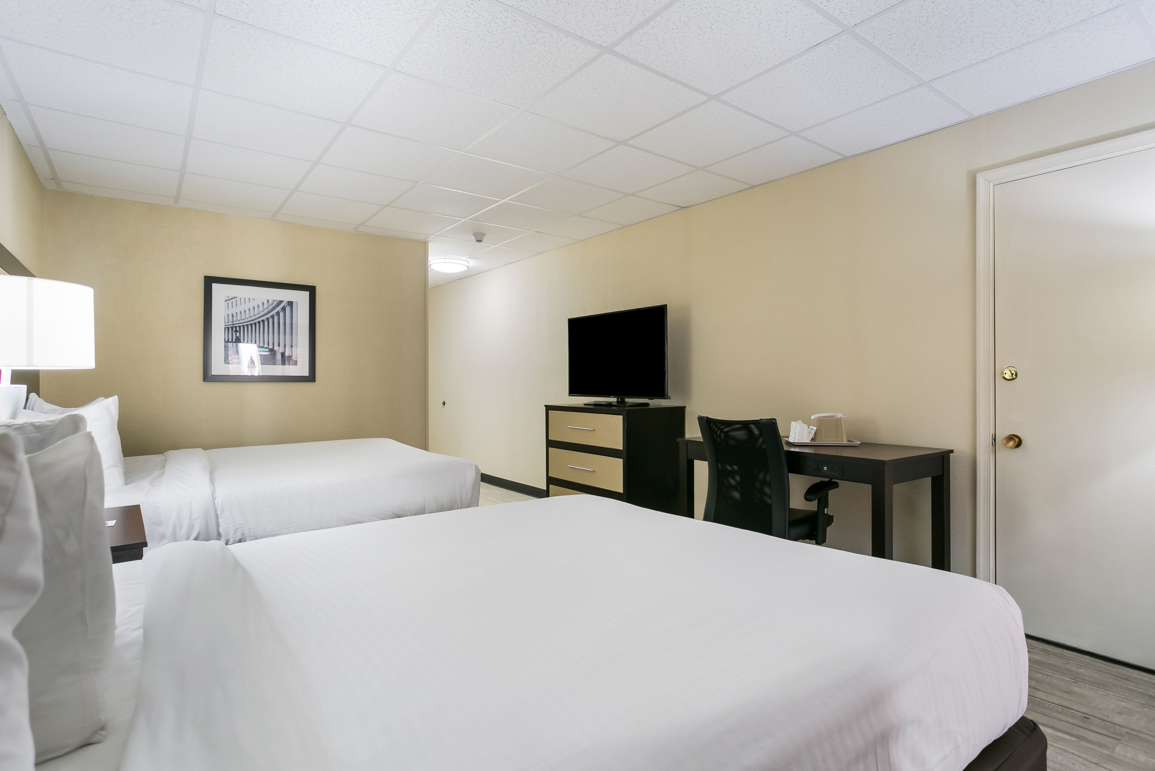 A hotel room with two beds, a desk, a chair, a television, and a door.