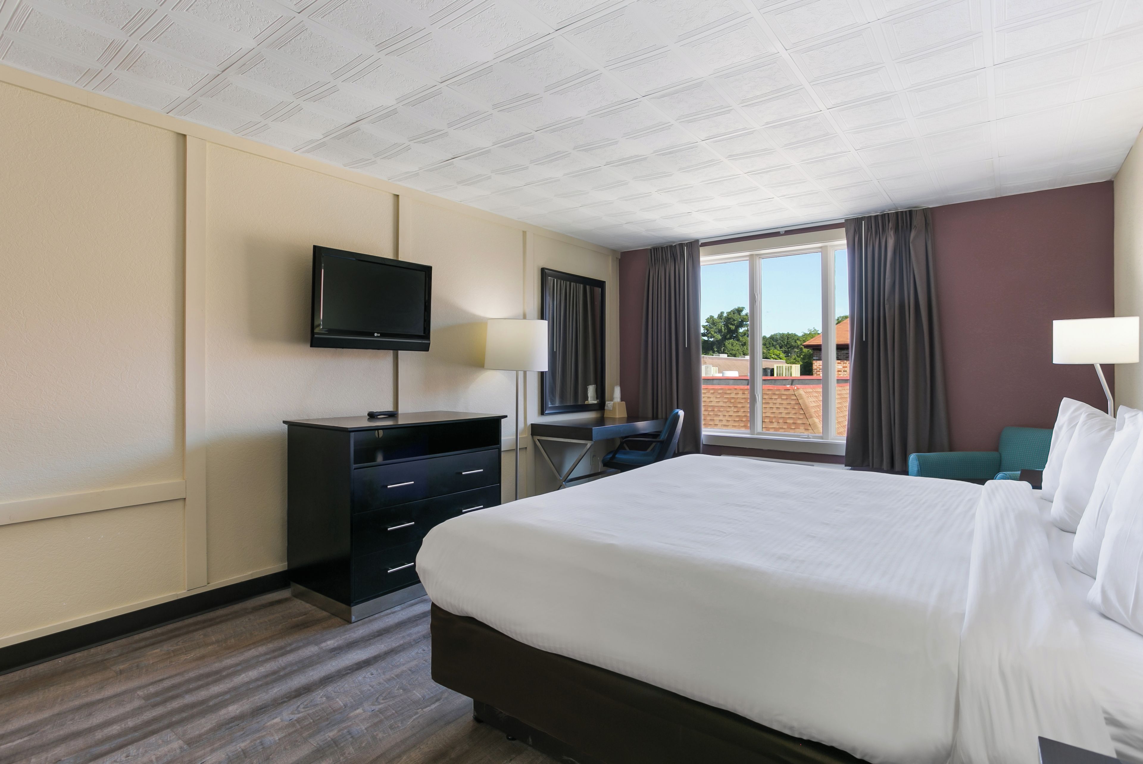 A hotel room with a bed, a desk, a television, and a window with curtains.