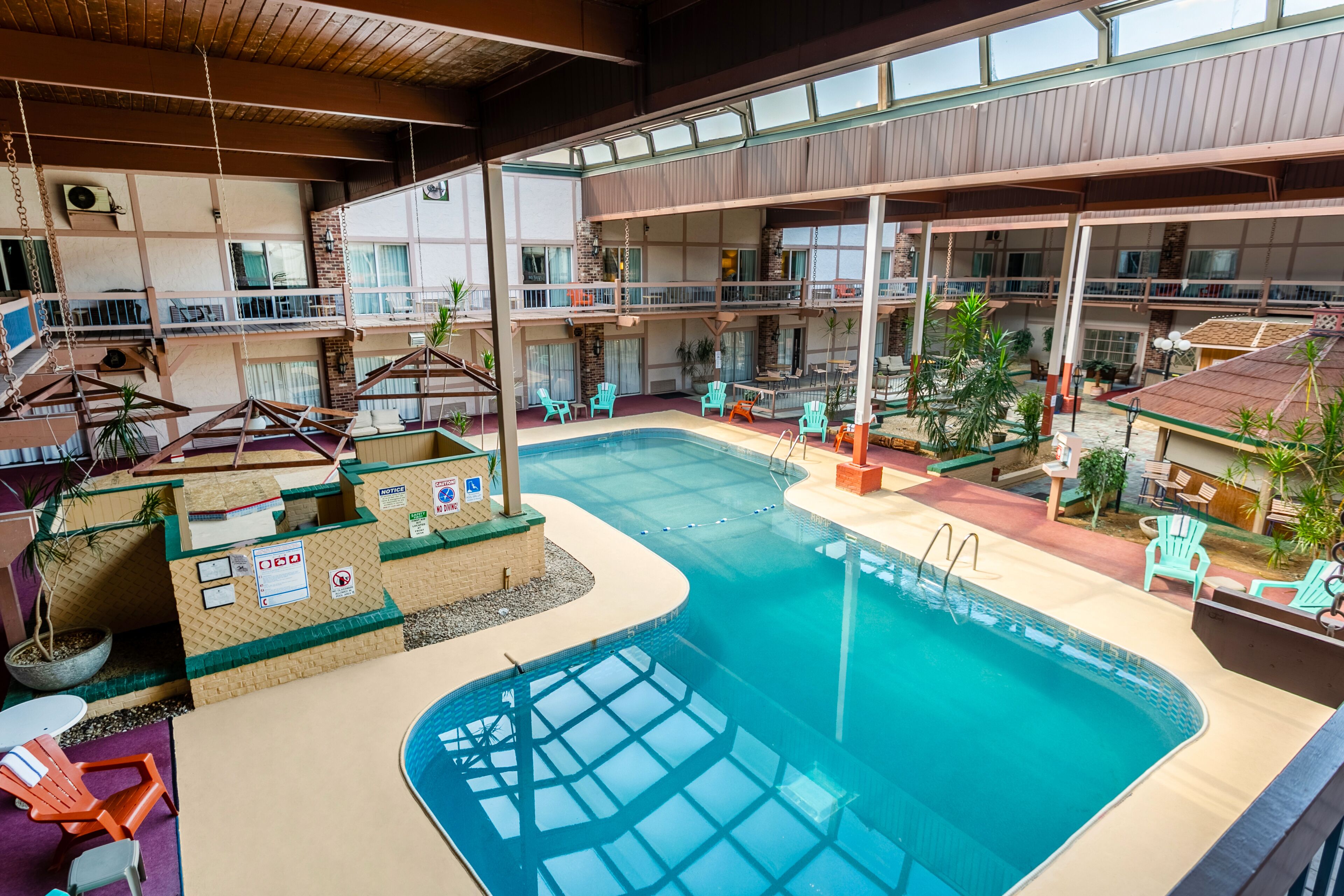 An indoor swimming pool with multiple levels of balconies, surrounded by seating areas and potted plants.