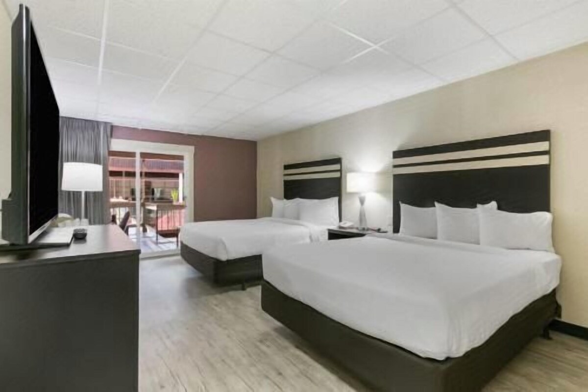 A hotel room with two beds, a TV, and a desk with a lamp.