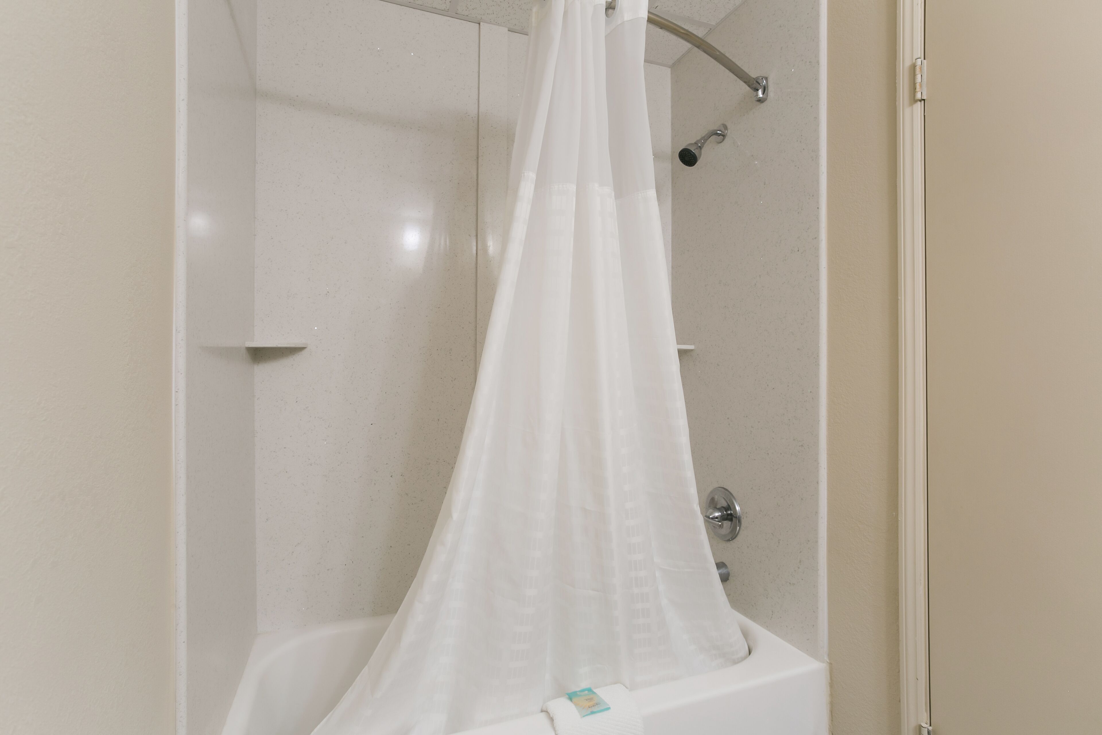 A shower area with a white shower curtain and a handheld showerhead.