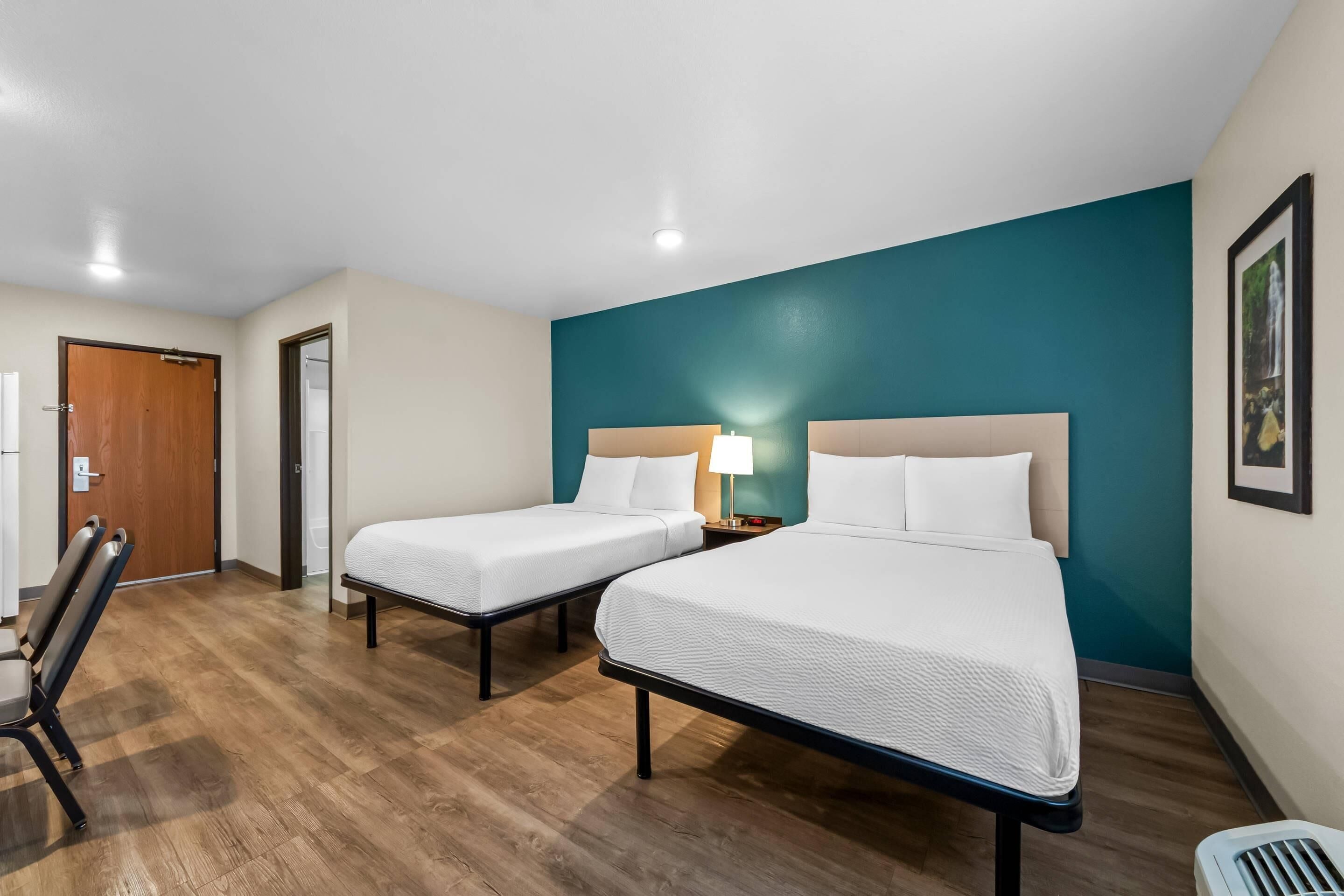 Ein Hotelzimmer mit zwei Einzelbetten, Holzboden, einer Wand in Türkis und einer weißen Tür.