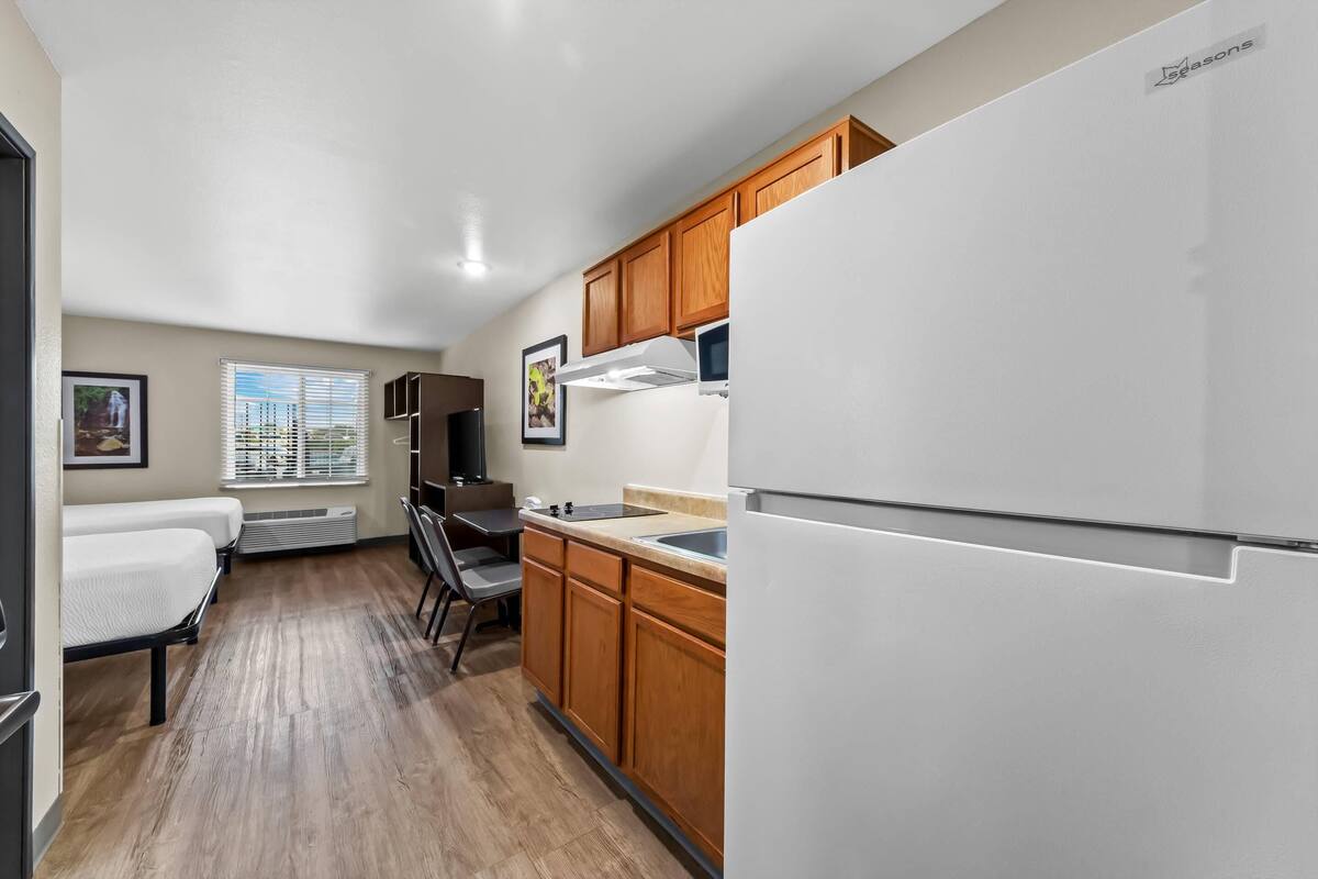 A compact kitchen with wooden cabinets, a white refrigerator, and a dining area with a table and chairs.