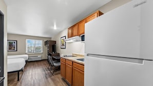 Cocina compacta con armarios de madera, un refrigerador blanco y una zona de comedor con mesa y sillas.