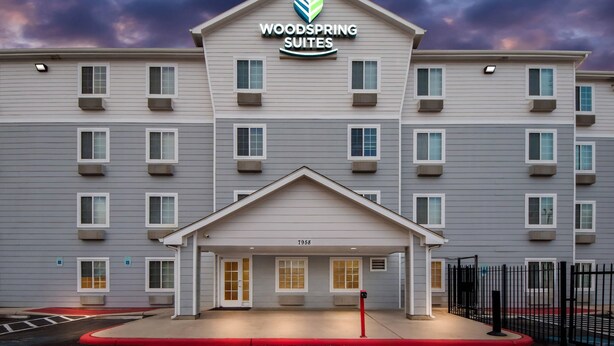 Un hotel de varios pisos con techo plano, entrada central y un letrero que dice "WOODS SPRING SUITES".