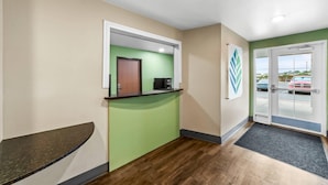 Un área de recepción con una pared verde, suelo de madera, un mostrador de recepción y una puerta que da al exterior.