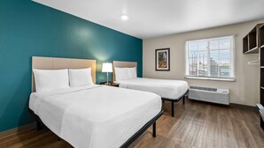 Habitación de hotel con dos camas, una pared de acento color aguamarina, un ventanal con persianas, un cuadro en la pared y un calentador empotrado.