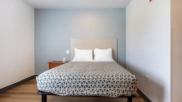 A neatly made bed with a geometric-patterned bedspread, a wooden nightstand, and a wall-mounted light fixture.
