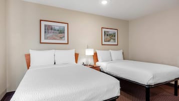 Una habitación de hotel con dos camas, una mesita de noche con lámpara y dos cuadros en la pared.