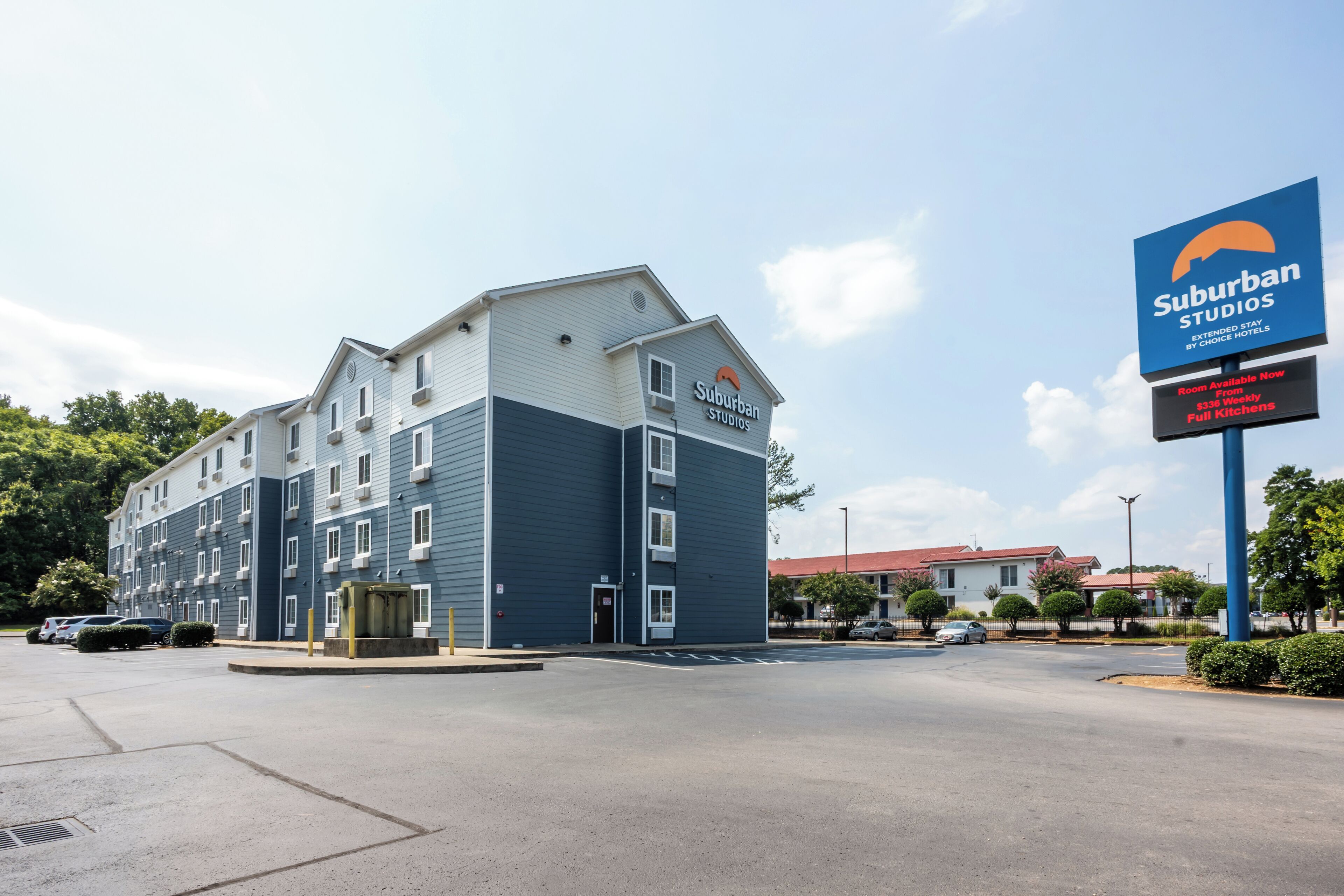 Un immeuble à plusieurs étages, portant l’enseigne « Suburban Studios », qui présente un design architectural moderne avec un toit plat et une façade aux couleurs bleu et blanc.