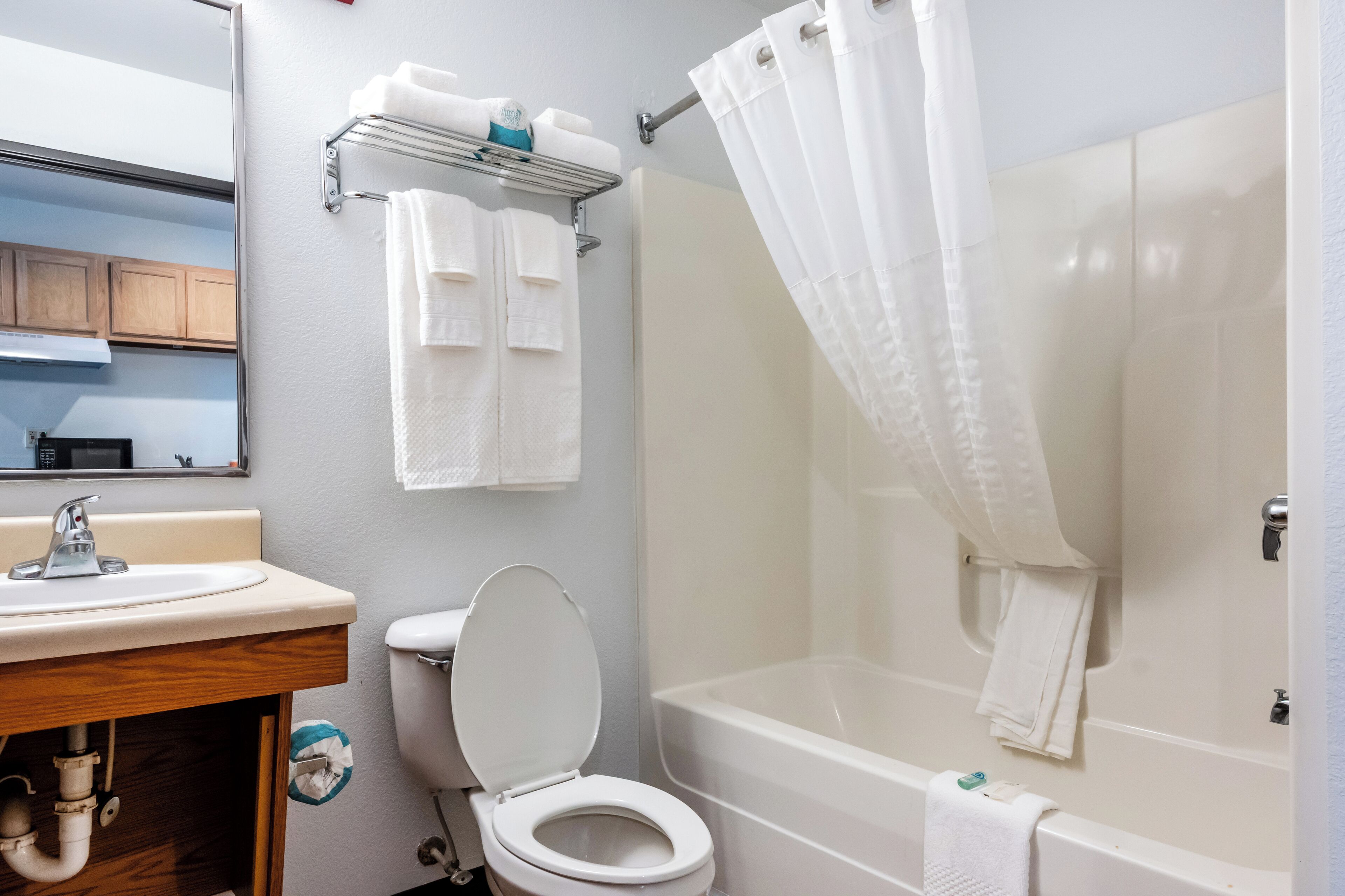 Un baño con inodoro, lavamanos y bañera. Hay toallas colgadas en un perchero y una cortina de ducha.