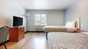 Een slaapkamer met een bed, een televisie op een dressoir, een raam en een stoel.