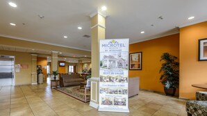 Un vestíbulo de hotel con una zona de recepción, una planta grande en maceta y un expositor promocional de Microtel Inn & Suites.