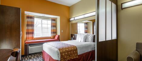 A hotel room with a bed, a window with curtains, a desk, and a chair.
