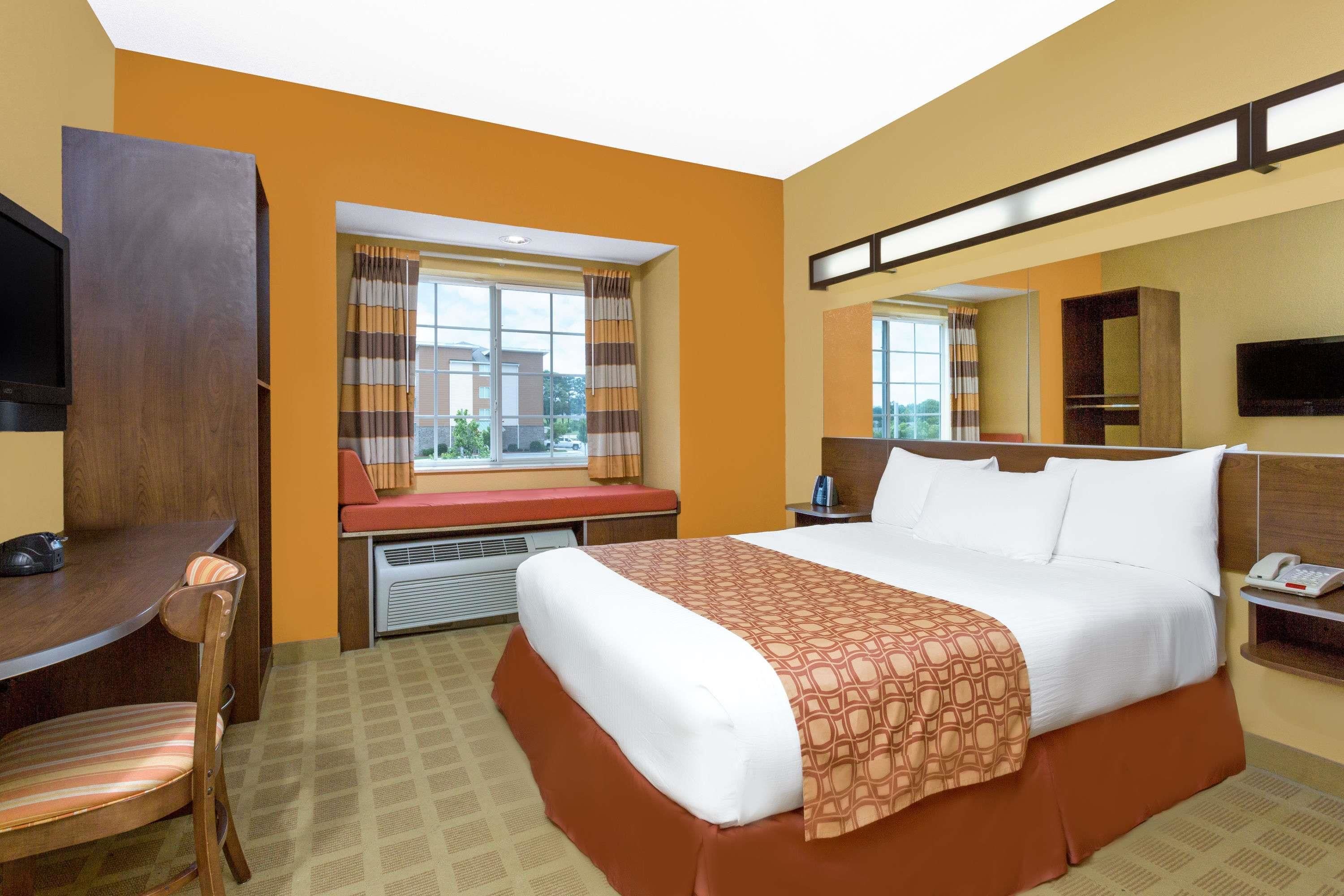 Habitación de hotel con cama, escritorio, silla, ventana con cortinas, calefacción, televisión y teléfono.