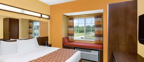 A hotel room with a large bed, a window with curtains, a bench, a TV, and a wardrobe.