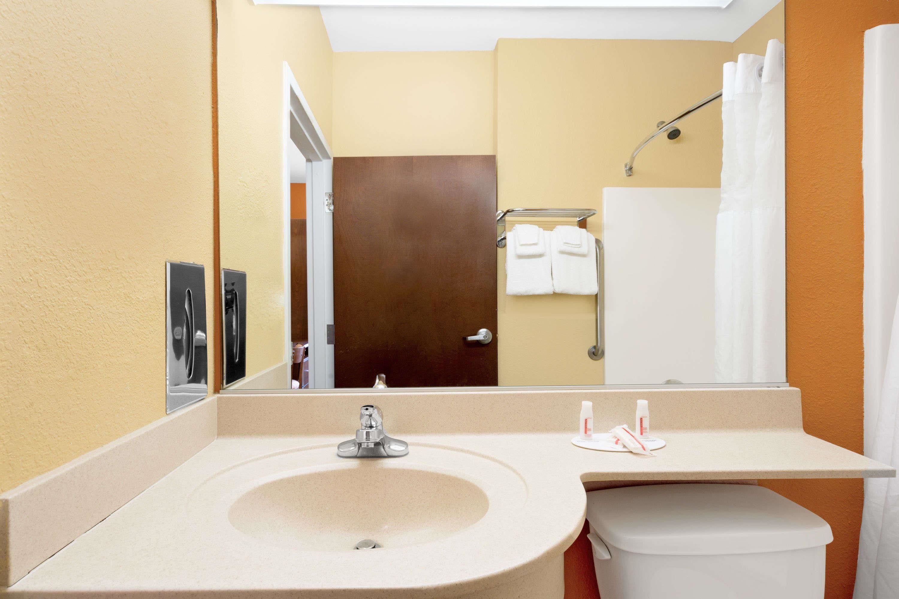 Baño con lavamanos, inodoro y espejo que refleja una puerta y un perchero.