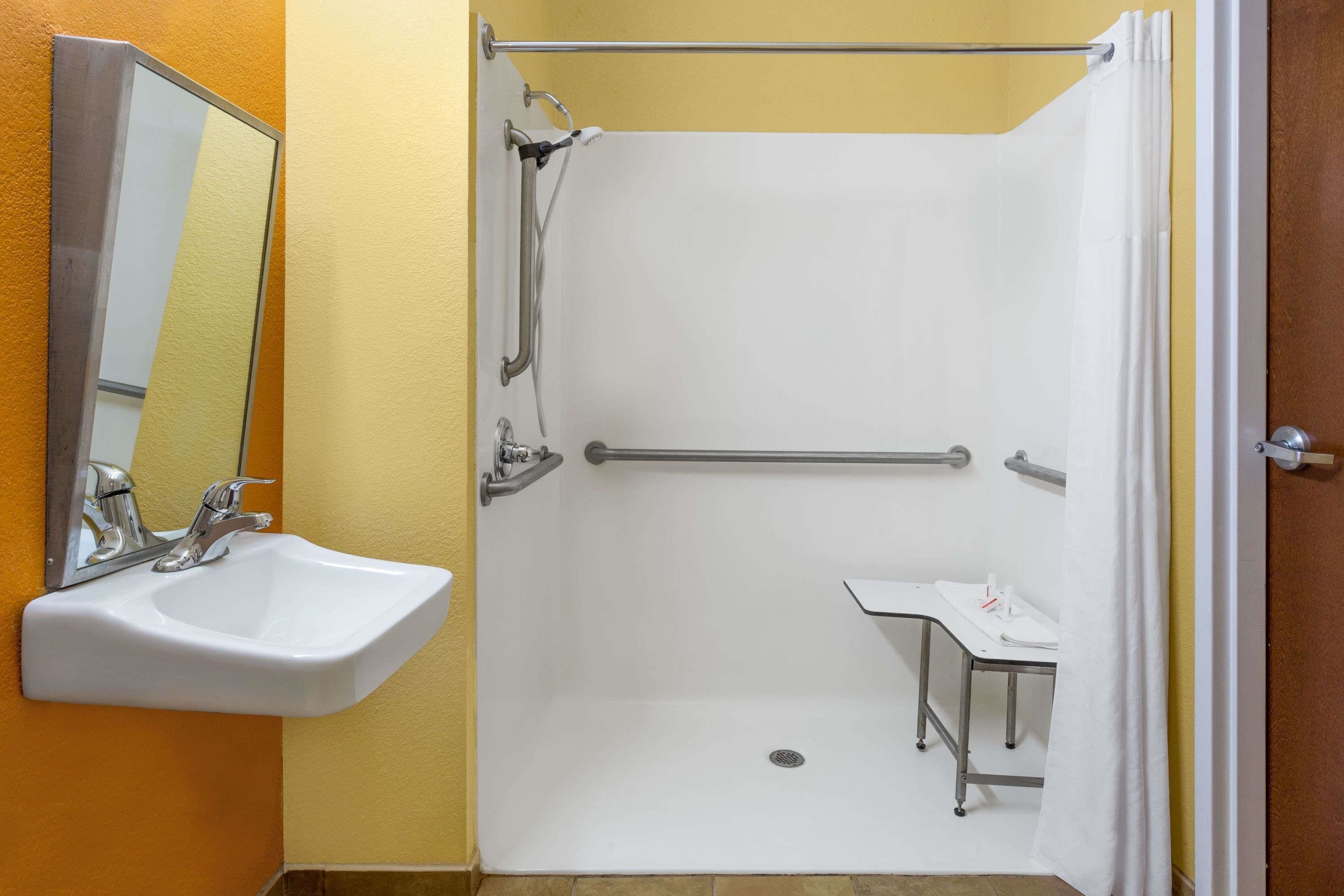 A bathroom with a white sink, a shower with a grab bar, and a small vanity table.