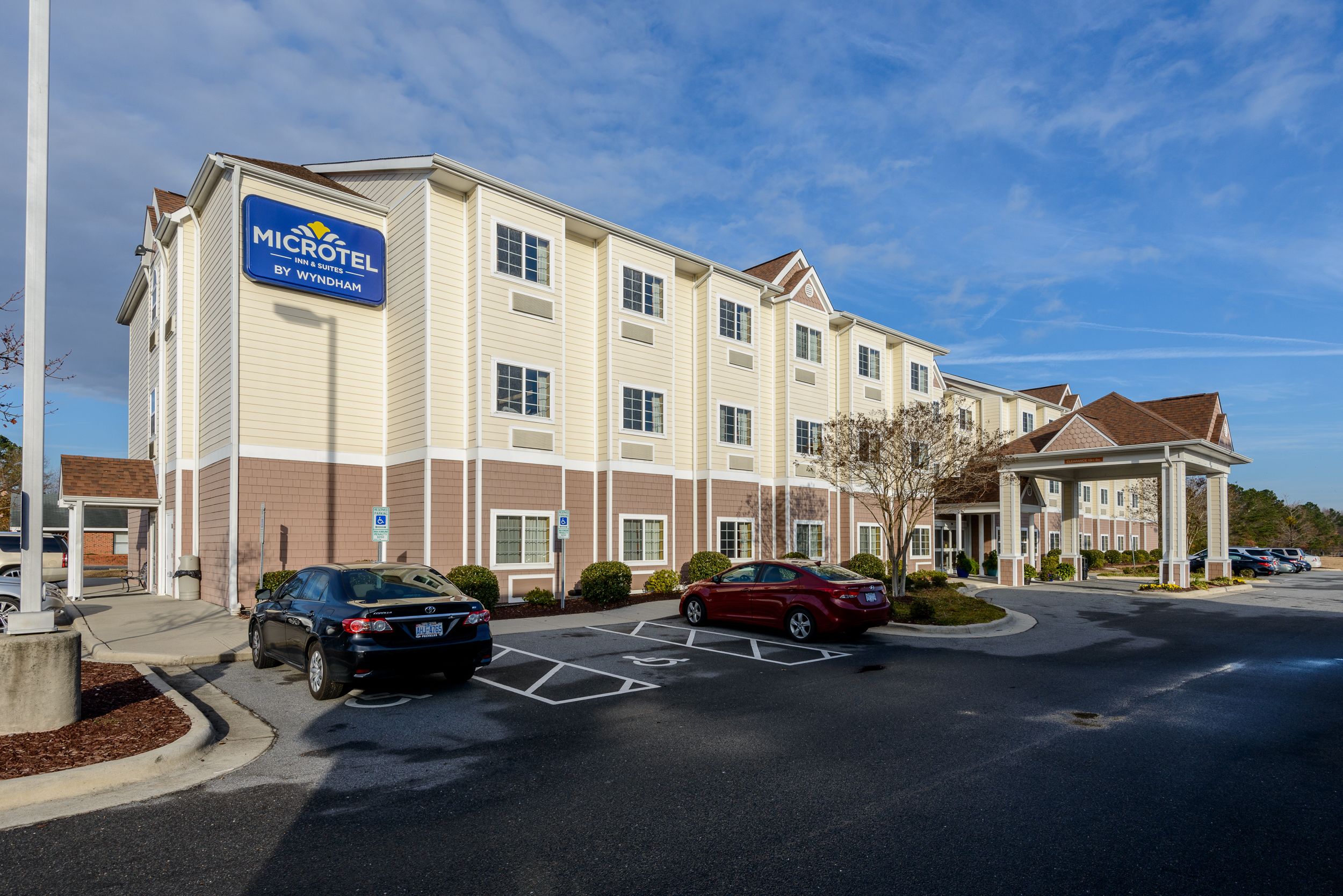 Edificio de Microtel Inn & Suites by Wyndham con un estacionamiento y dos autos estacionados al frente.