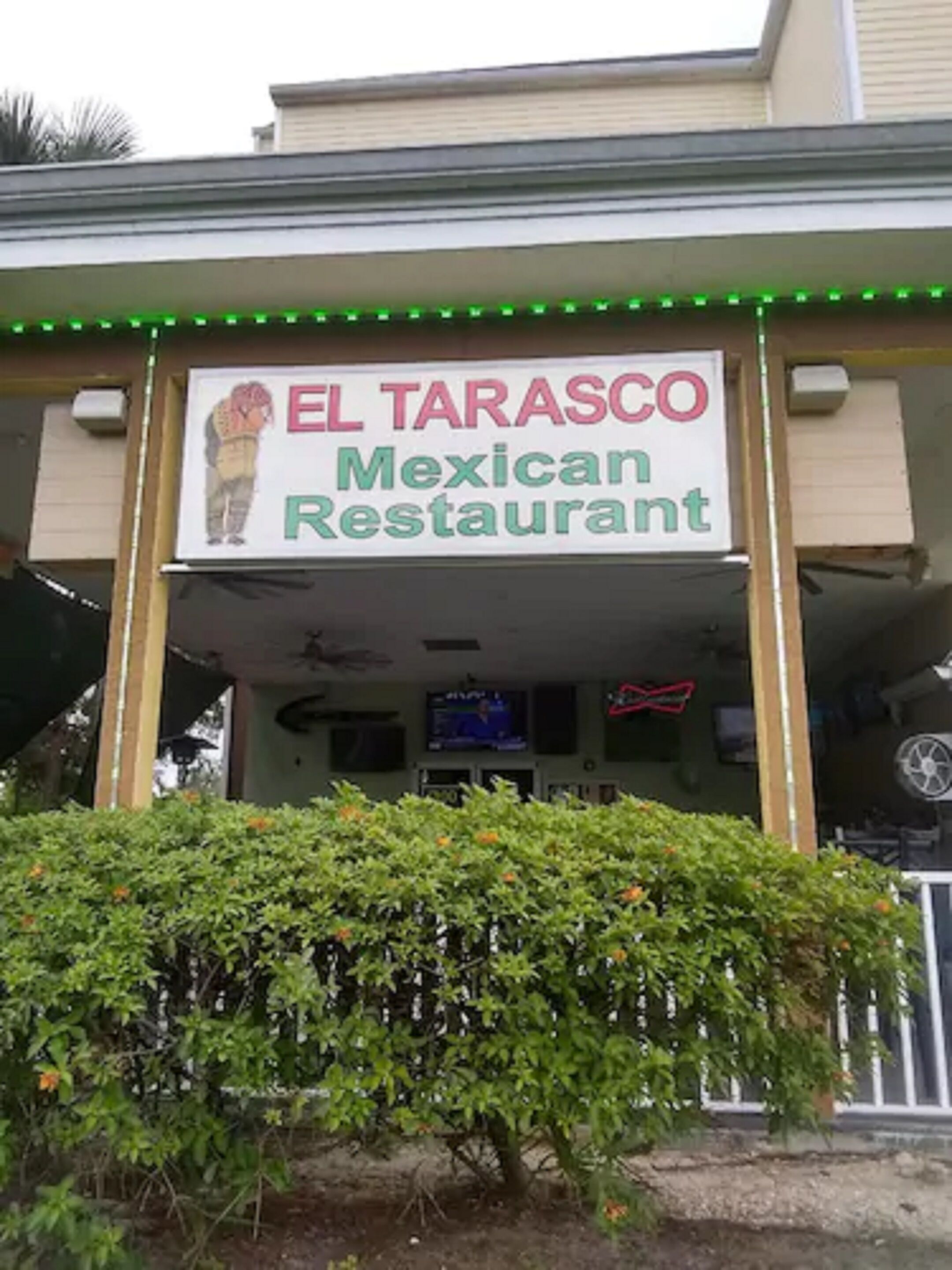 The exterior of El Tarasco Mexican Restaurant with a signboard, green LED lights, and a small garden area in front.