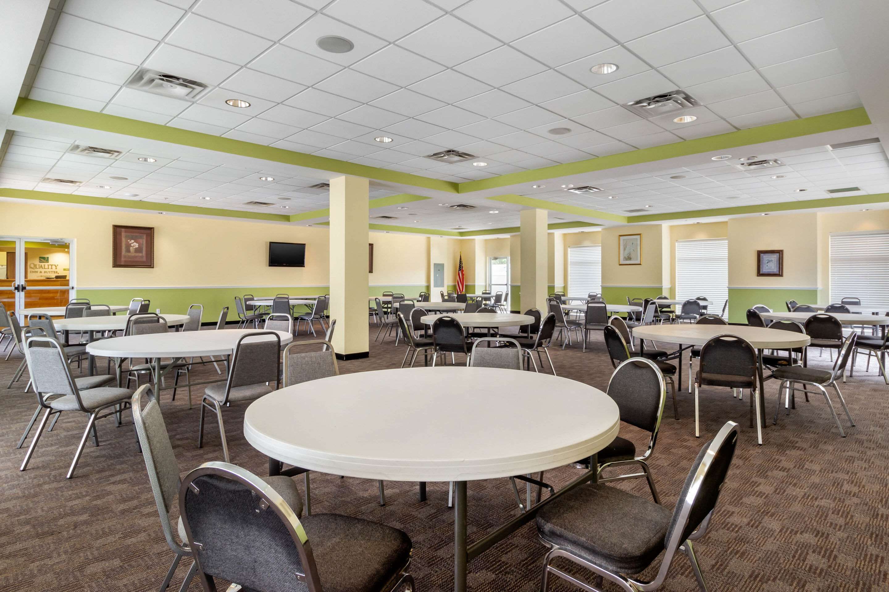 A conference room with multiple tables and chairs, a ceiling with recessed lighting, and a framed picture on the wall.