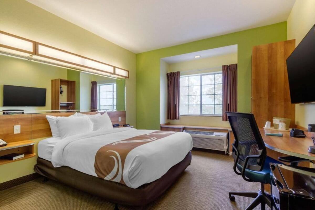 A hotel room with a bed, desk, chair, television, and a window with curtains.