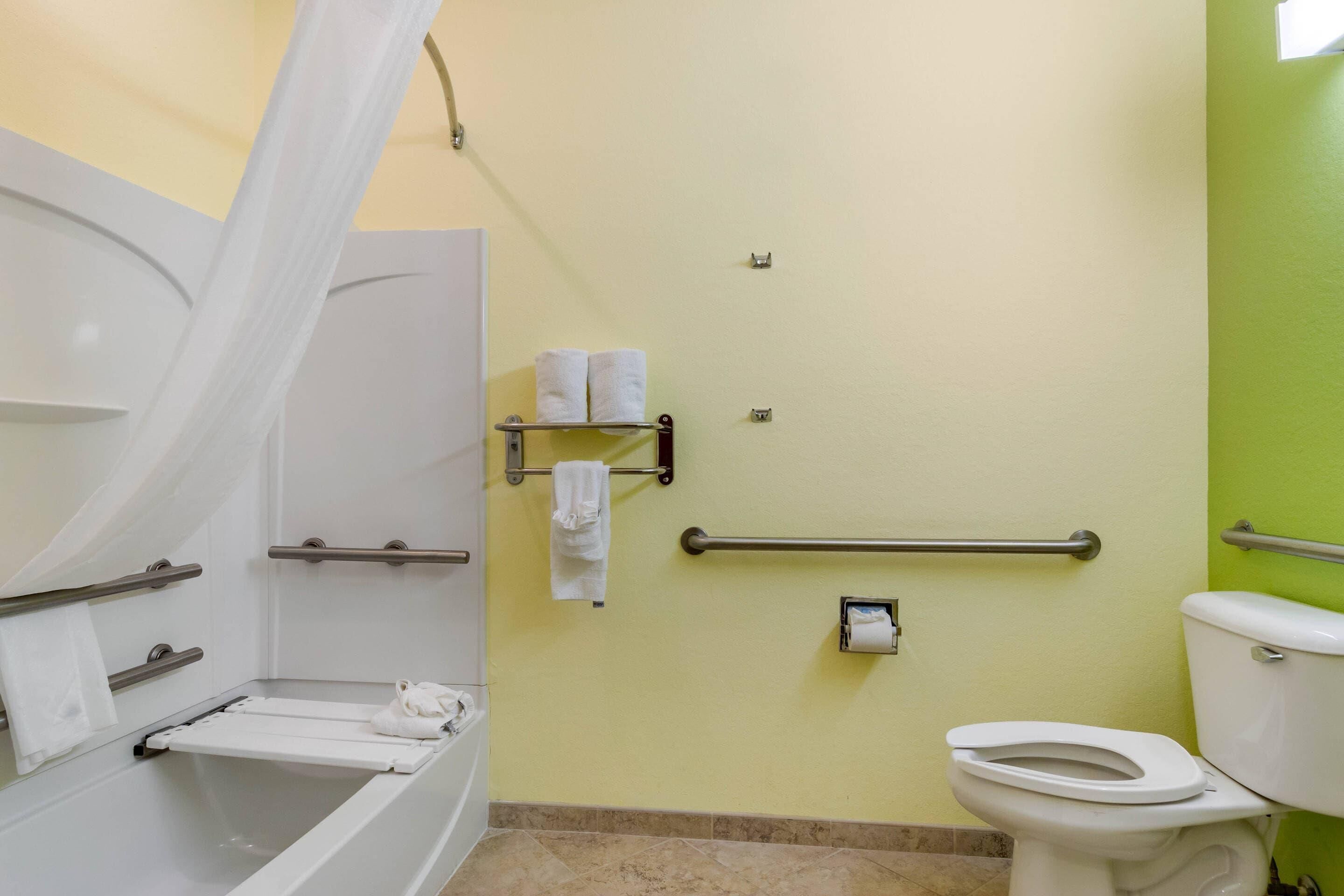A bathroom with a bathtub, toilet, and handrails.