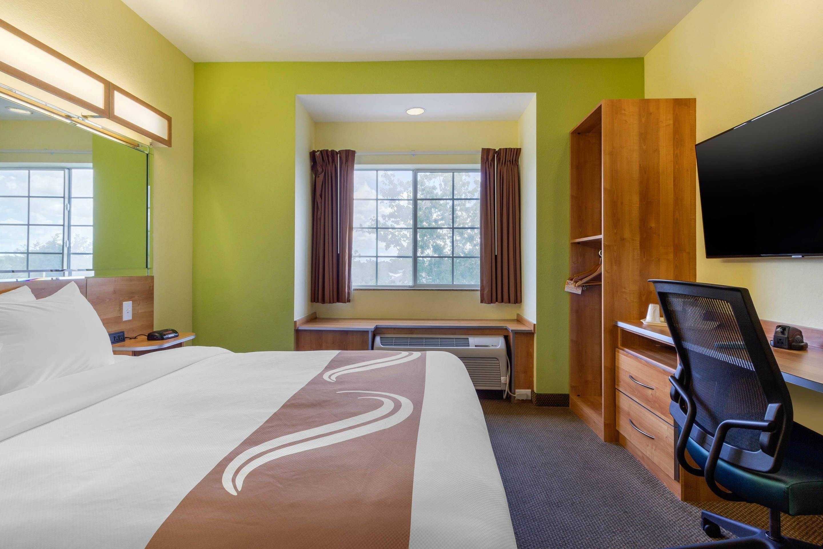 A hotel room with a bed, a desk, a chair, a TV, and a window with curtains.
