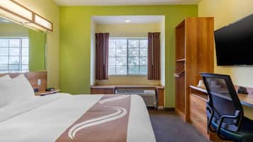 A hotel room with a bed, a desk, a chair, a TV, and a window with curtains.
